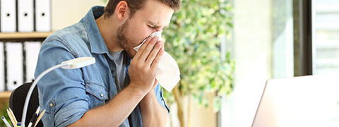 Man sneezing over his computer desk